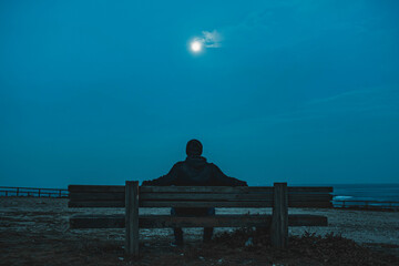 A man sitting in a bench at night