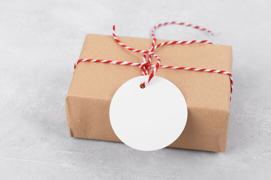 Round empty gift tag mockup on gift kraft box, Christmas simple blank paper label with string on gift box on grey background