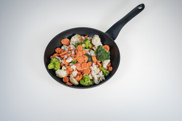 Frozen vegetables in a frying pan on a light background .Background, top view. There is a place for text .Cabbage, carrots.