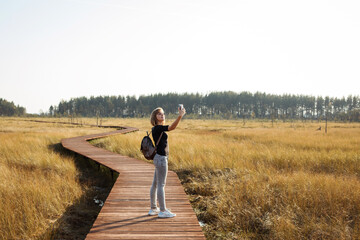 European woman is taking selfie while walking on the eco path over the swamp, ecological tourism.