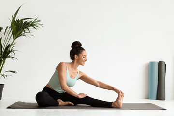 Fototapeta premium Beautiful Young Woman Stretching Legs On Yoga Mat In Light Studio