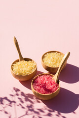 Wooden bowls with a spoon filled with pink and yellow bath sea salt. Beauty treatment for spa and wellness on pink background. Skincare natural cosmetic concept for body care