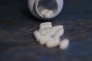 Pastillas blancas en un bote con pastillas enfrente derramadas encima de la mesa