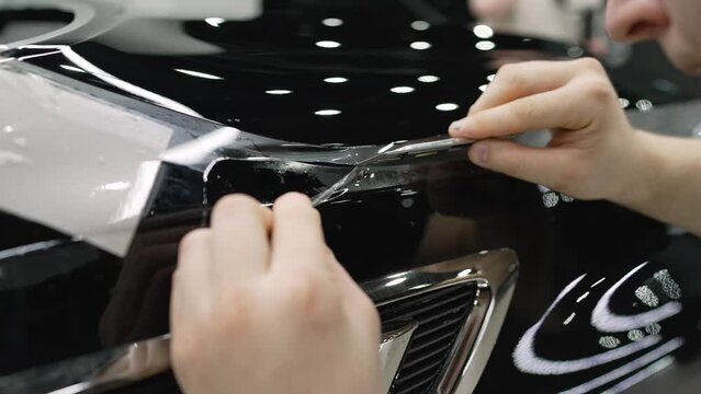 Photographing a car body in a car service. Car detailing. The protective film is cut with a knife on the car.