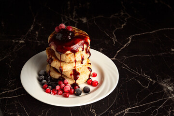Pancakes are stacked, pouring syrup over frozen berries