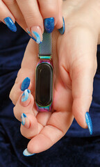 Female hands with a multicolored manicure and smart watches on dark blue background closeup