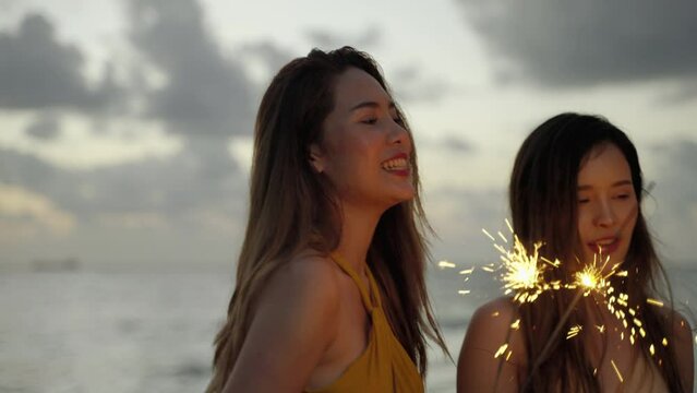  beautiful Shea woman and her friends are having fun playing sparklers on the beach during Twilight.
