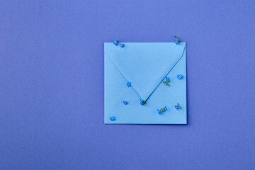 Beautiful forget-me-not  flowers with kraft blue envelope on blue background with space for text. Happy Mother's Day, St. Valentine’s day greeting card. Flat lay.