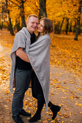 Obraz premium Young couple is walking in the sunny autumn park. Happy boy and girl are rolling themselves in the rug near yellow tree. Fallen yellow leaves, brith warm autumn weather. Autumn love story in park 