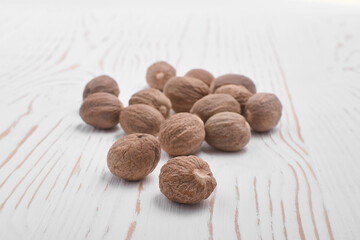 heap of dried nutmeg on white wooden background