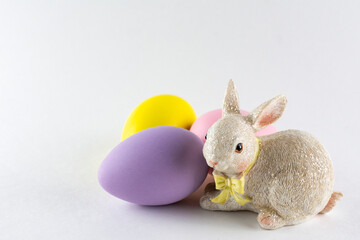 Fototapeta na wymiar Easter bunny figurine with three Easter eggs on white background with copy space.