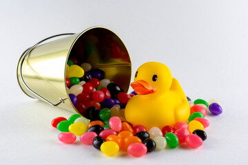 A rubber duck surrounded by assorted jelly beans from spilled pail.  White background with copy space.