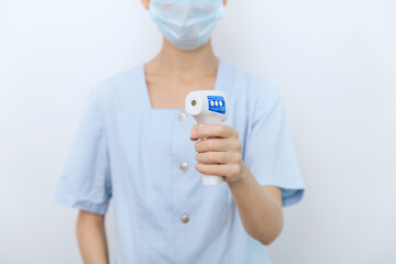Temperature measurement gun in doctor hands. Close-up shot of doctor wearing protective surgical mask ready to use infrared isometric thermometer gun to check body temperature for virus symptoms.