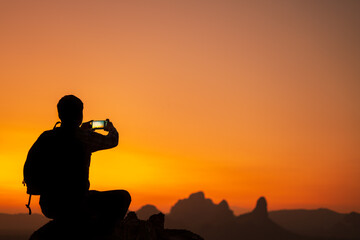 Fototapeta na wymiar Silhuette of photographer traveler taking photo by smart phone with beautiful sunset from top of the mountain