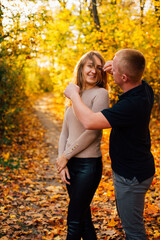 Fototapeta premium Young couple is having a walk in the sunny autumn park, forest. Happy man and his woman are hugging . Fallen yellow leaves, brith warm autumn weather. Autumn love story in park 
