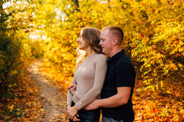 Young couple is having a walk in the sunny autumn park, forest. Happy man and his woman are hugging . Fallen yellow leaves, brith warm autumn weather. Autumn love story in park
