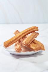 Traditional churros with sugar and cinnamon served on a marble table, with a bowl of caramel...