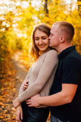 Fototapeta premium Young couple is having a walk in the sunny autumn park, forest. Happy man and his woman are hugging . Fallen yellow leaves, brith warm autumn weather. Autumn love story in park 