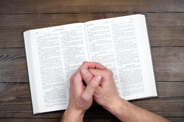 Naklejka premium Prayer. Open Bible. Hands folded in prayer. The man is praying. Hands on the table.