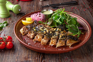 Grilled baked mackerel served with sauce, lemon and green salad on wooden table