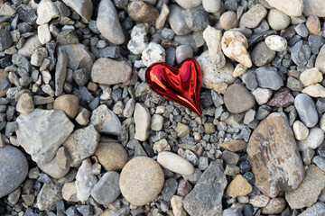 top view of red shiny heart in middle of colorful pebble stones outdoor.