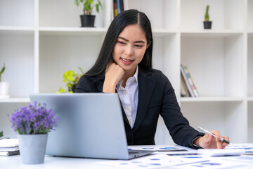 Asian businesswoman working on tablet and taking notes, accountant use a computer laptop at work in the office.