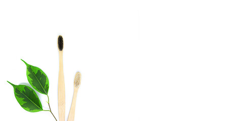 eco-friendly bamboo toothbrushes in black and white and a twig with green leaves lie on a white background. Flat lay, top view. Copy space. Zero waste personal care product, dental care