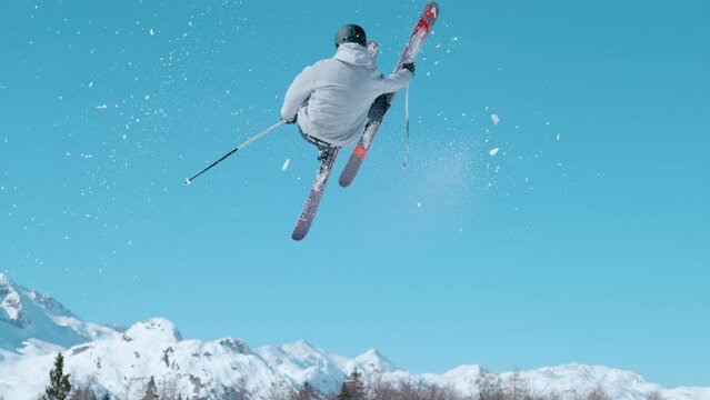 SLOW MOTION TIME WARP: Cinematic action shot of a male skier jumping off a large kicker. And doing a trick. Freestyle skier does a breathtaking spinning trick while exploring the fun park slopes.