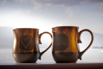 coffee tea mugs with heart and word love, romantic Valentines card backdrop in brown chocolate tones with lake background