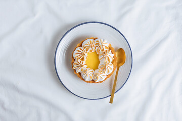 Lemon tart decorated with wiped cream. Decorated with flowers and different cloths and golden spoon. Lemon custard cream and sweet dough.