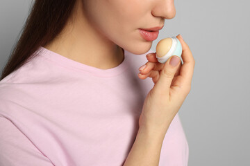 Young woman applying lip balm on grey background, closeup - obrazy, fototapety, plakaty