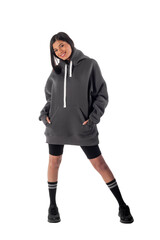 An attractive woman of Latin appearance wears a gray hooded hoodie on a white background. The girl looks sexy and happy. The elegant brunette is wearing a dark sweatshirt. All-season clothing