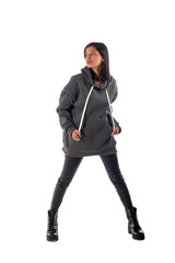 An attractive woman of Latin appearance wears a gray hooded hoodie on a white background. The girl looks sexy and happy. The elegant brunette is wearing a dark sweatshirt. All-season clothing