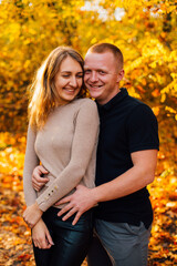 Young couple is having a walk in the sunny autumn park, forest. Happy man and his woman are hugging . Fallen yellow leaves, brith warm autumn weather. Autumn love story in park
