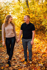 Young couple is having a walk in the sunny autumn park, forest. Happy man and his woman are hugging . Fallen yellow leaves, brith warm autumn weather. Autumn love story in park
