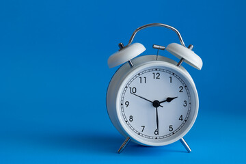 Isolated white alarm clock on a vibrant blue background with copy space