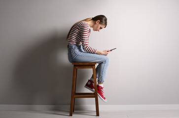 Woman with bad posture using tablet while sitting on stool near light grey wall indoors - obrazy, fototapety, plakaty