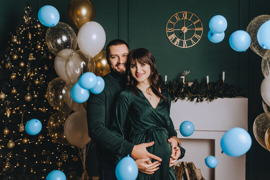 A stylish, bearded man and a cute, beautiful pregnant brunette girl are hugging against the background of flying blue balloons in honor of the boy. Gender party.
