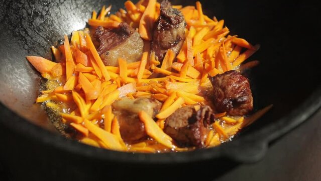 Carrots and meat are fried in oil in a cauldron