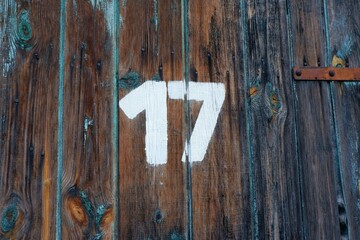 White colour number seventeen on an old abandoned weathered painted natural brown wooden gate of an old garage in Budapest suburb, Hungary
