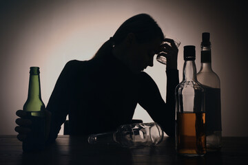 Alcohol addiction. Silhouette of woman with beer on wooden table, backlit