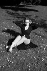 Black and white portrait of a young girl in the city park. Elegant and melancholy portrait, the girl is sitting on the grass. Beautiful woman in classic clothes