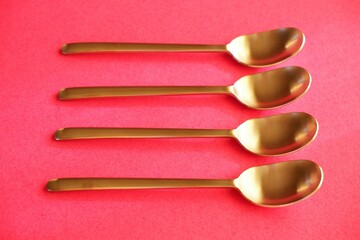 silver color small spoons side by side in a row on pink background