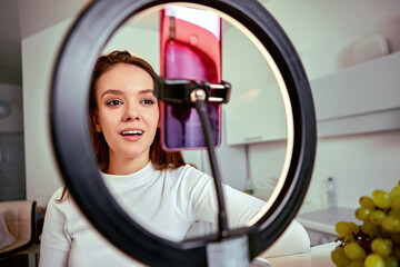 Makeup live streaming by woman using smartphone and ring light.