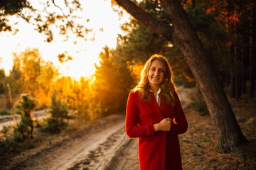 Elegant young girl at sunset in the forest. Stylish girl in a red coat and skirt. Warm autumn in the forest. Magic sunset and portrait of a girl
