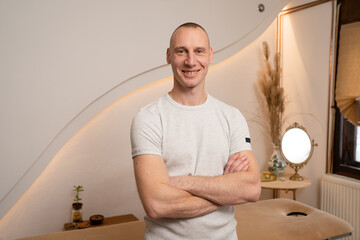 One man adult caucasian male standing at his massage studio with arms crossed confident looking to the camera short hair wearing white t-shirt masseur therapist - obrazy, fototapety, plakaty