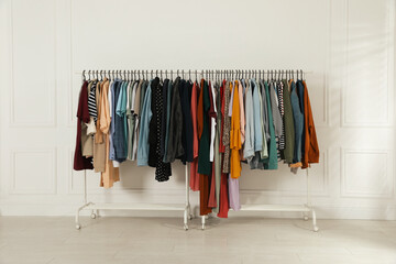 Racks with stylish clothes near white wall indoors. Fast fashion