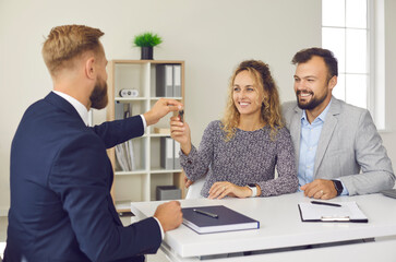 Family buys real estate. Male real estate agent at meeting in office hands over keys to his new...