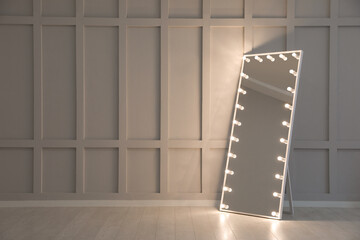 Modern mirror with light bulbs near molding wall in room, space for text