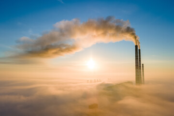 Aerial view of coal power plant high pipes with black smoke moving up polluting atmosphere at sunrise.